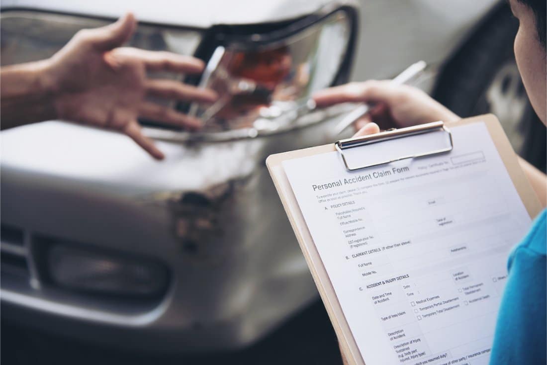 A close-up of a clipboard with a personal accident claim form and a damaged car in the background, highlighting the need for quick financial solutions like title pawns in Middleburg, FL.