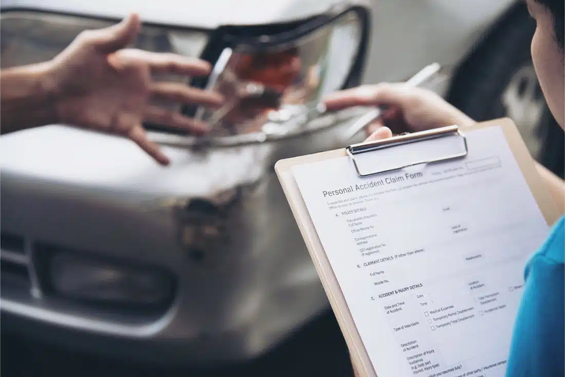 A close-up of a clipboard with a personal accident claim form and a damaged car in the background, highlighting the need for quick financial solutions like title pawns in Middleburg, FL.