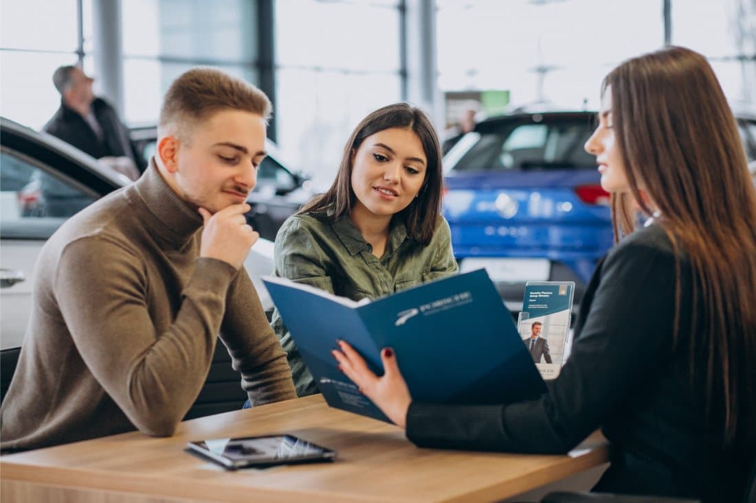 A young couple discussing financing options with a consultant at a car dealership, representing flexible title pawn solutions for Middleburg, FL residents.