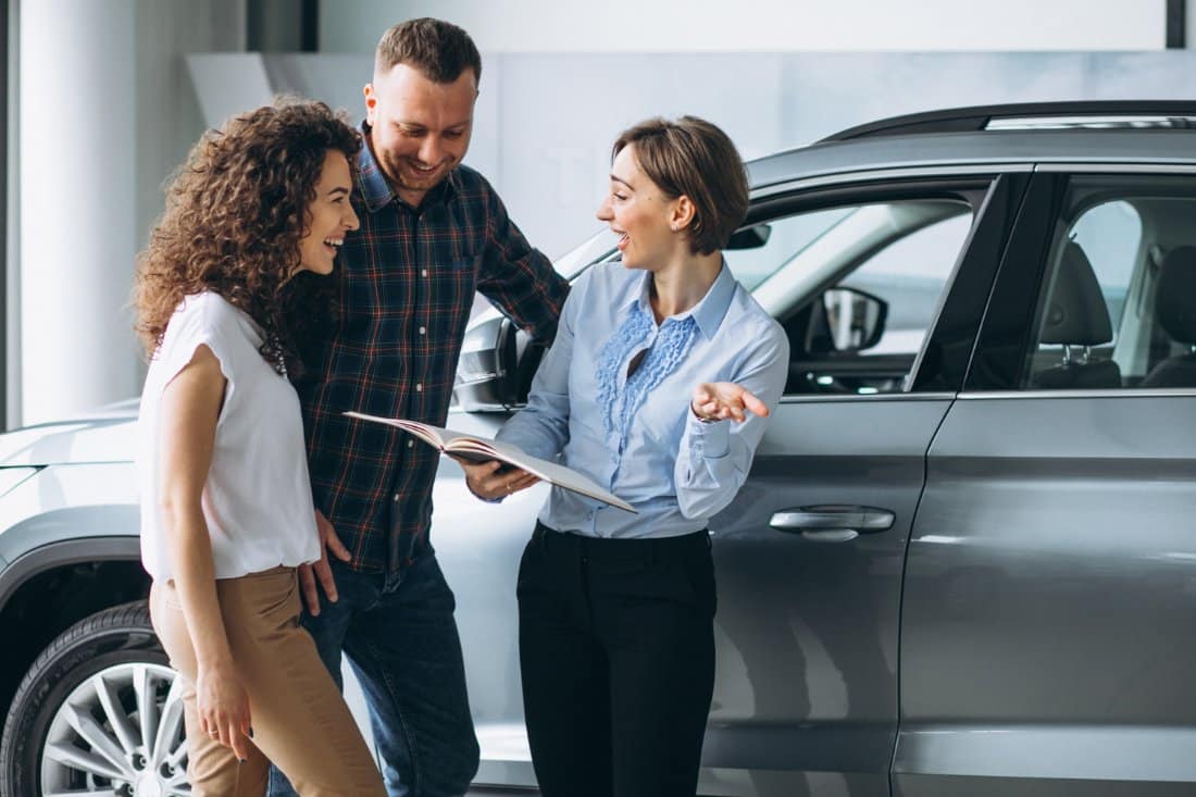 A couple discusses vehicle financing options with a sales representative inside a dealership, exploring quick cash solutions like title pawns in Clay County.