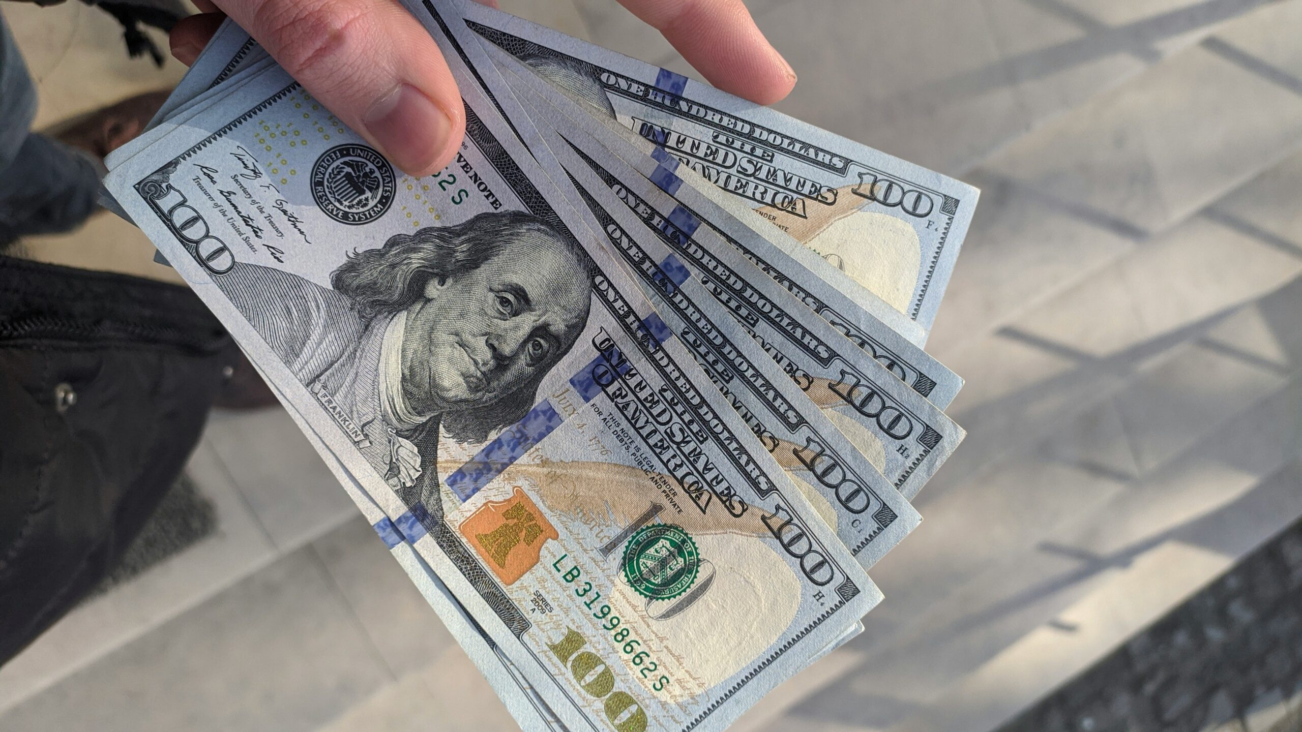 Person holding several US 100 dollar bills representing quick cash and loan payout.