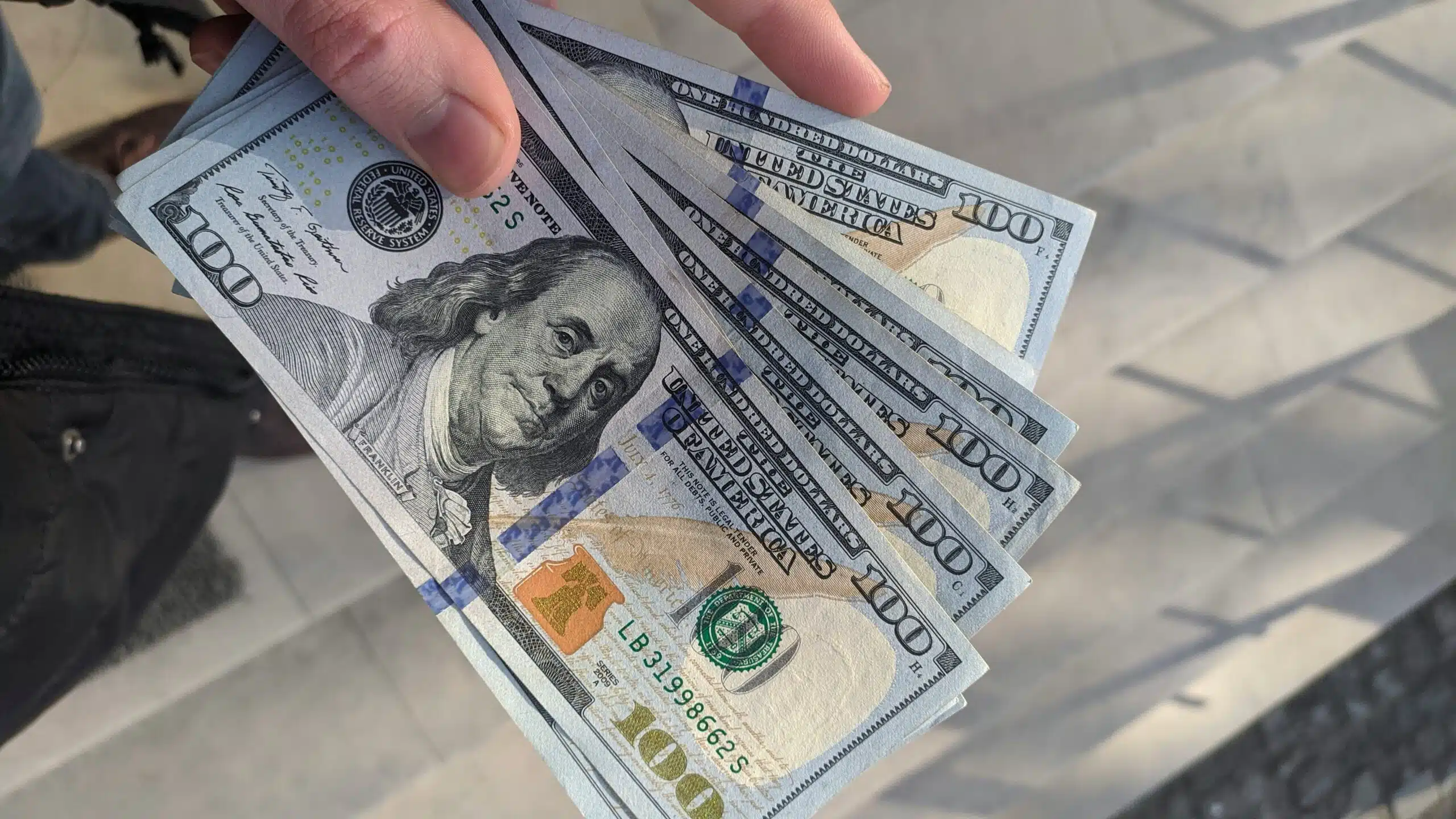 Person holding several US 100 dollar bills representing quick cash and loan payout.