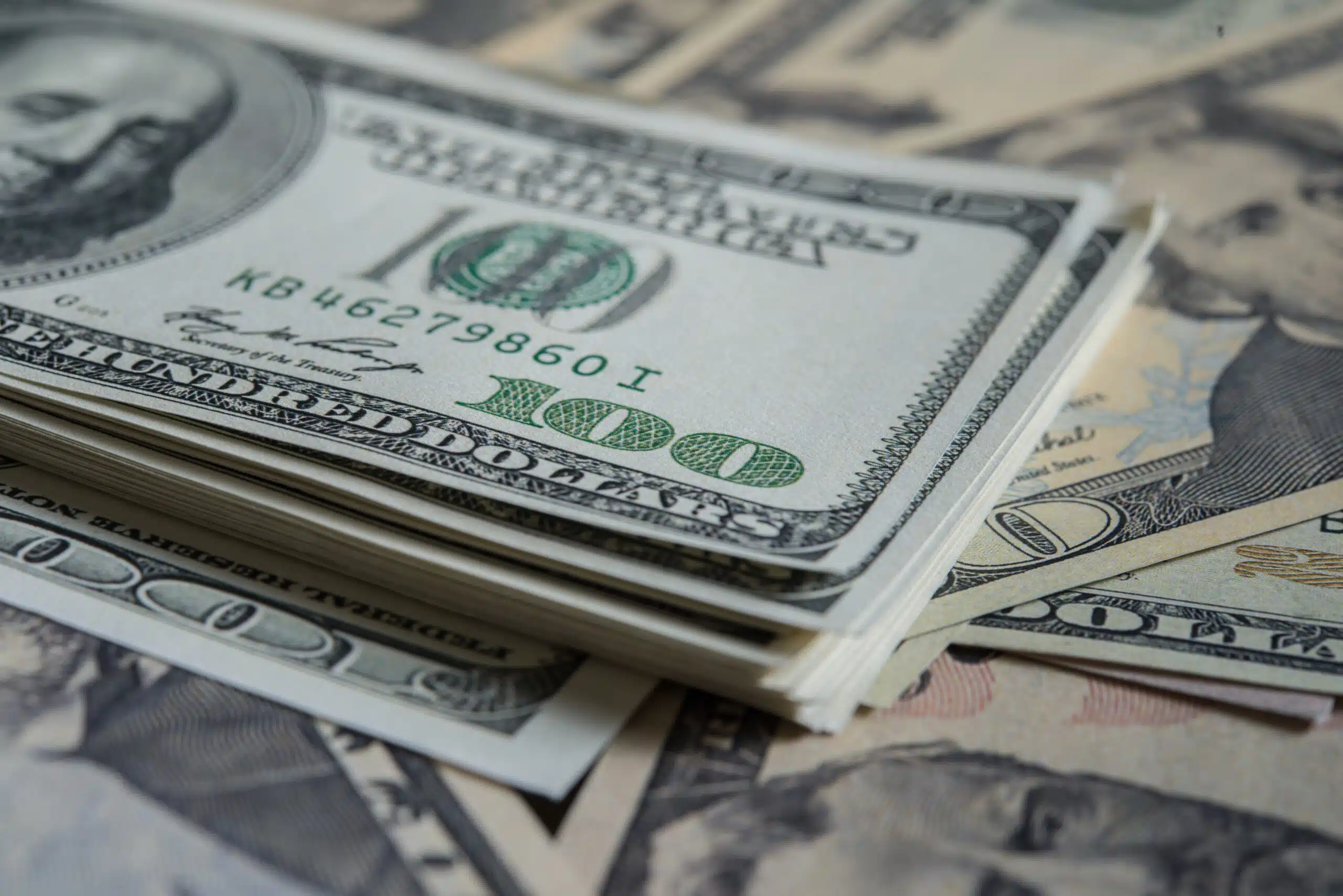 Close-up of a stack of 100-dollar bills on a surface covered with cash.