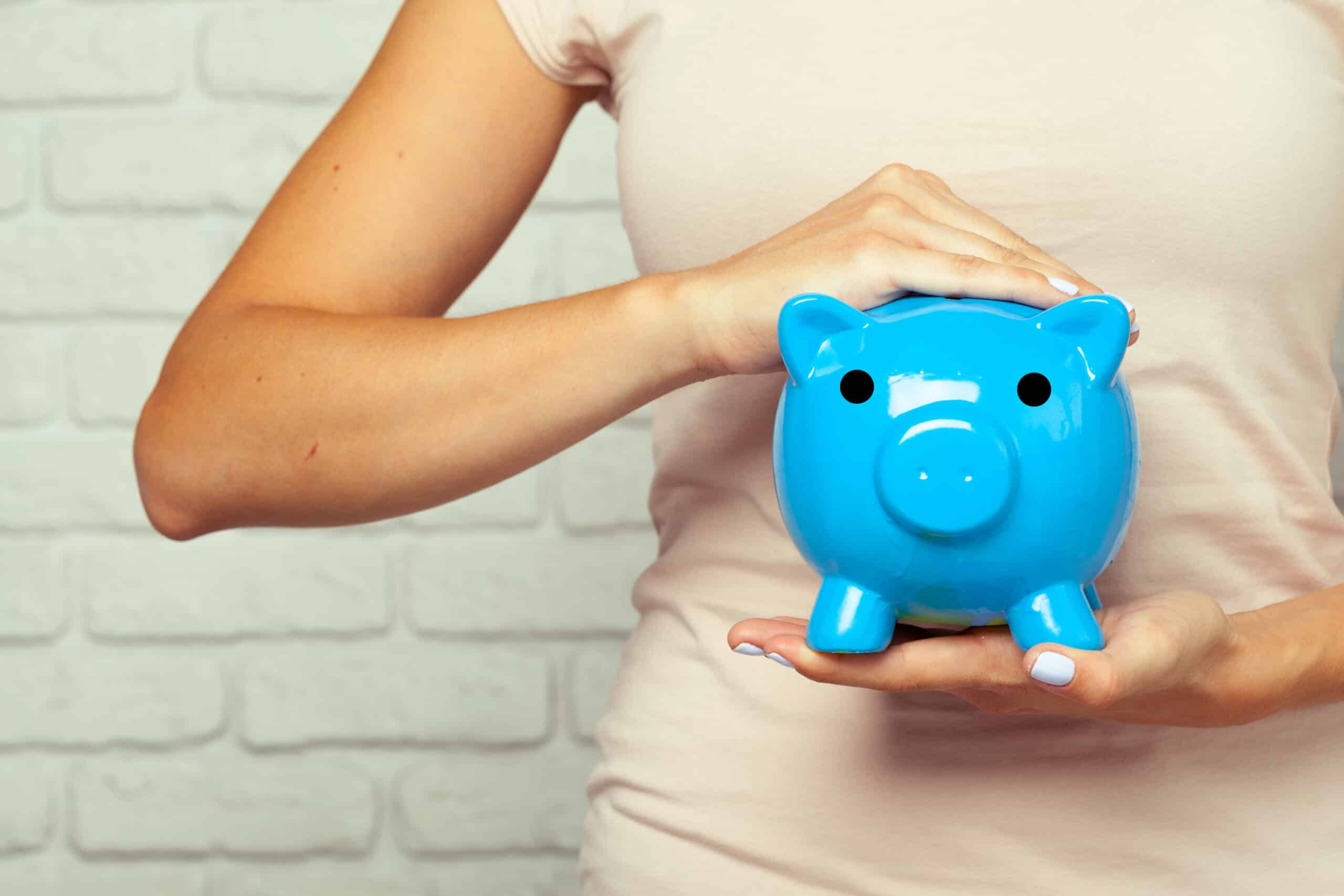 Person holding a blue piggy bank in front of a light-colored wall.