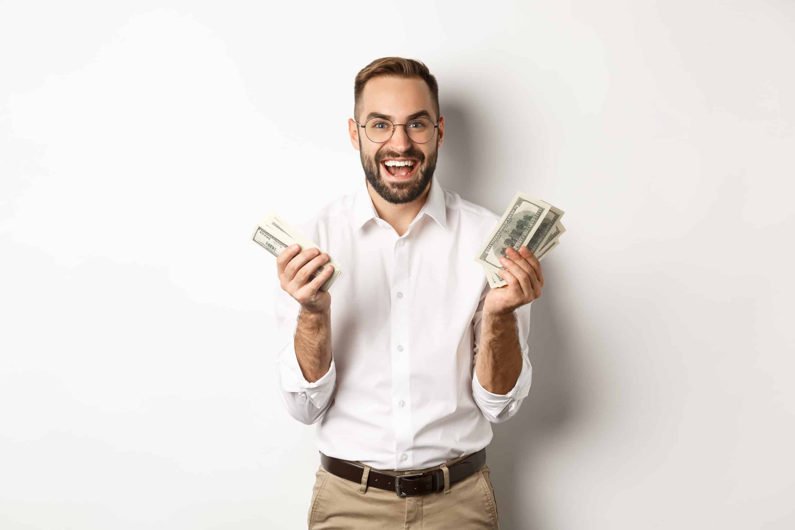 Man in a suit holding bills while posing next to a dog against a white background.